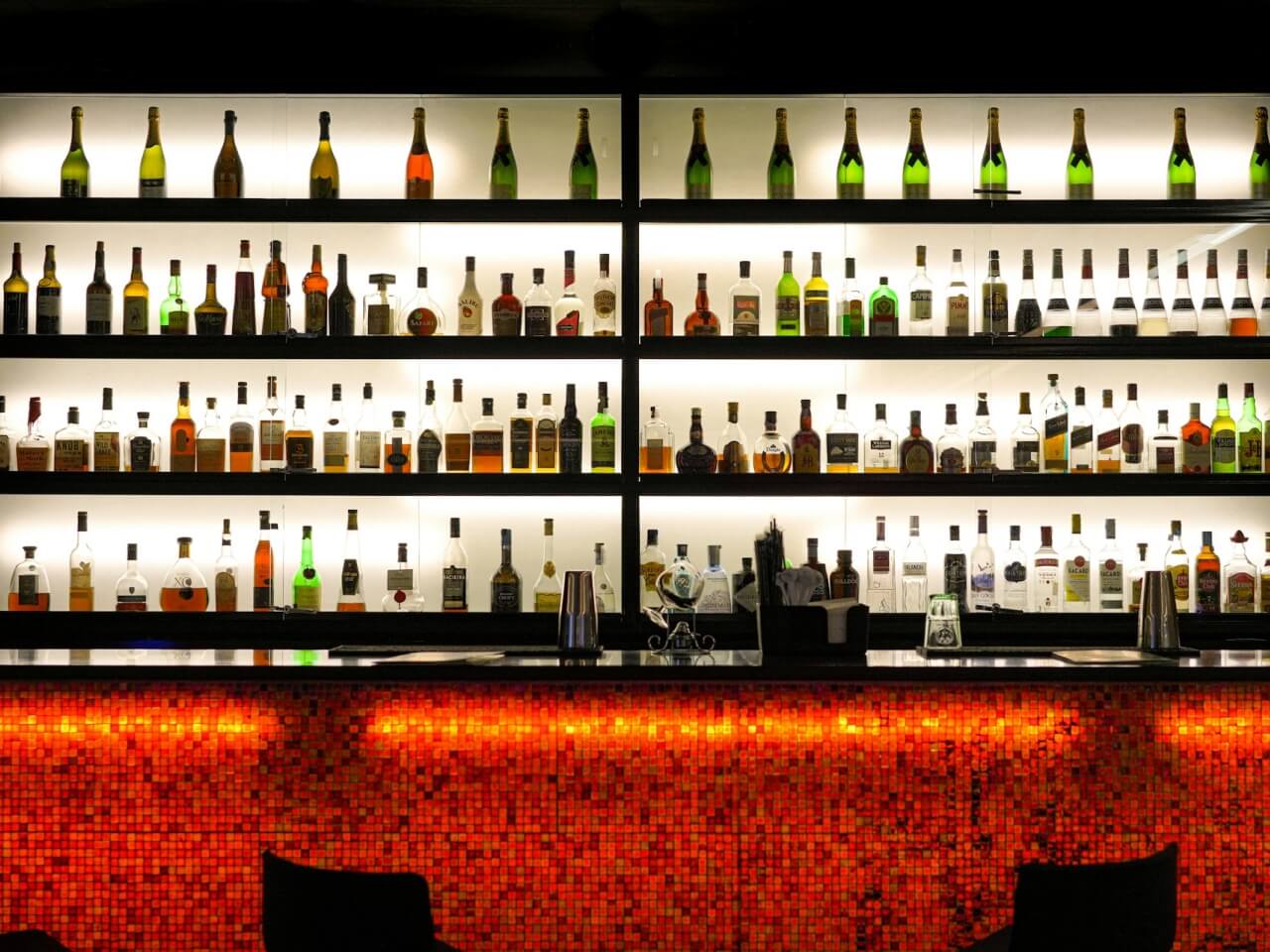 Backlit bar shelves lined with spirits and cocktail ingredients at a bar using Nommy for its online menu