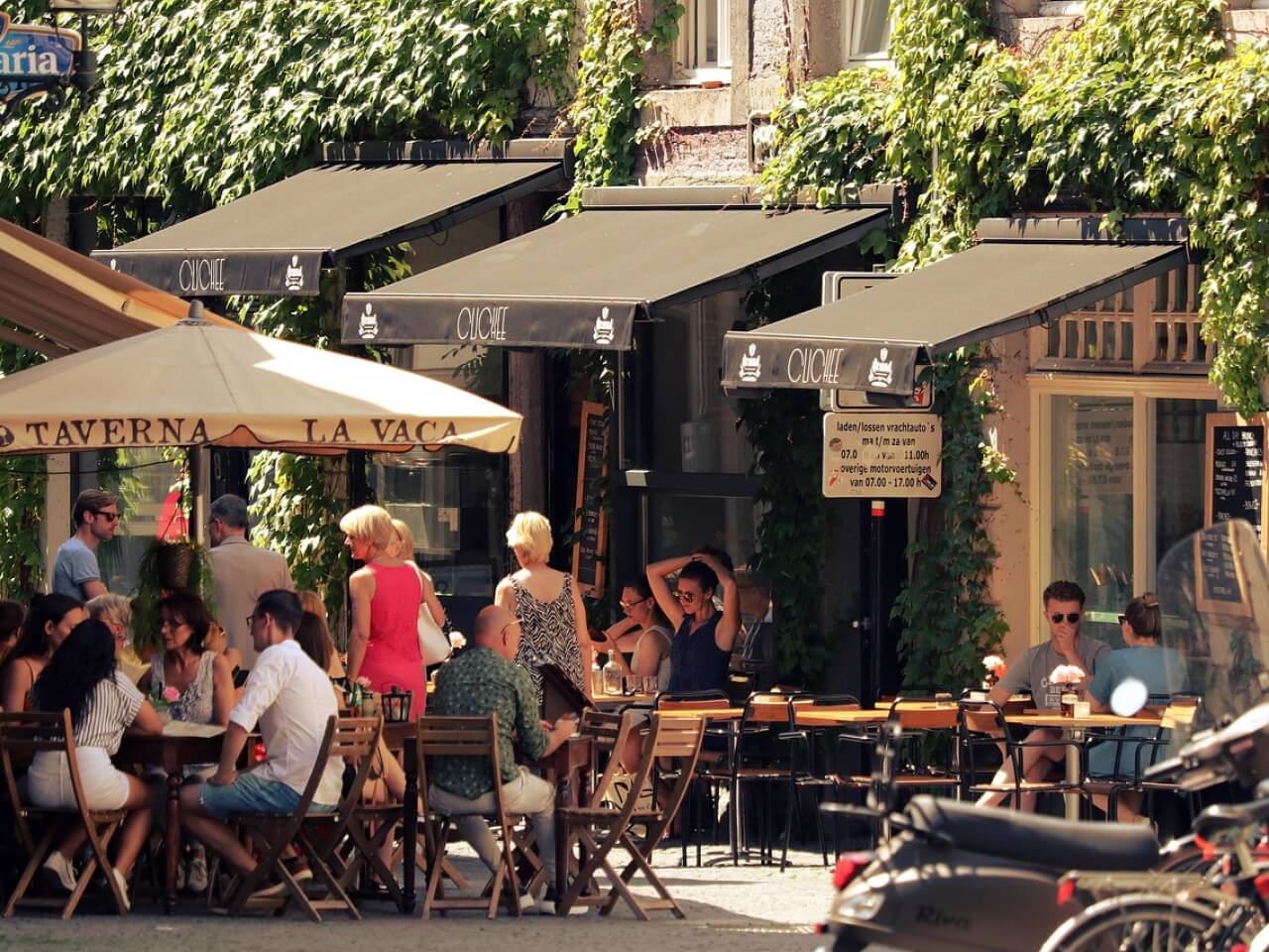 Sidewalk bistro terrace with ivy-covered walls, awnings, and diners seated outdoors