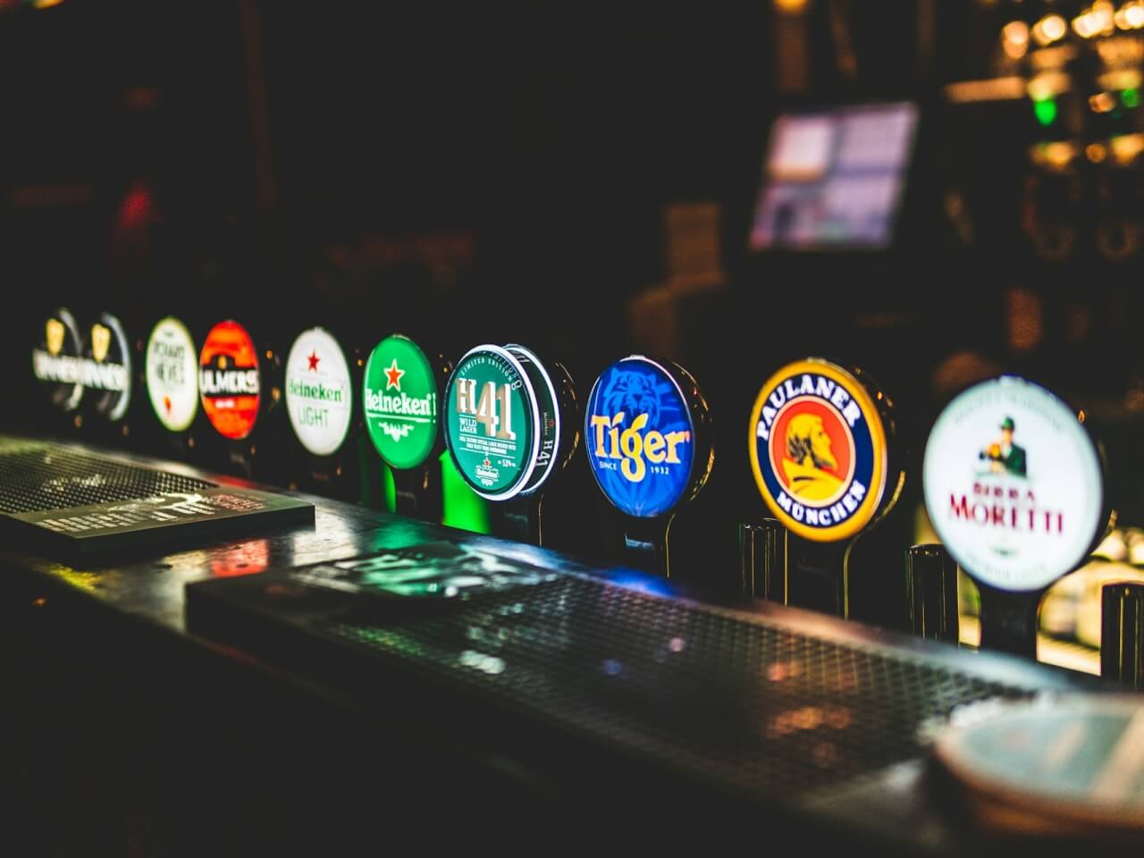 Row of illuminated beer tap handles lined up along a brewery taproom bar