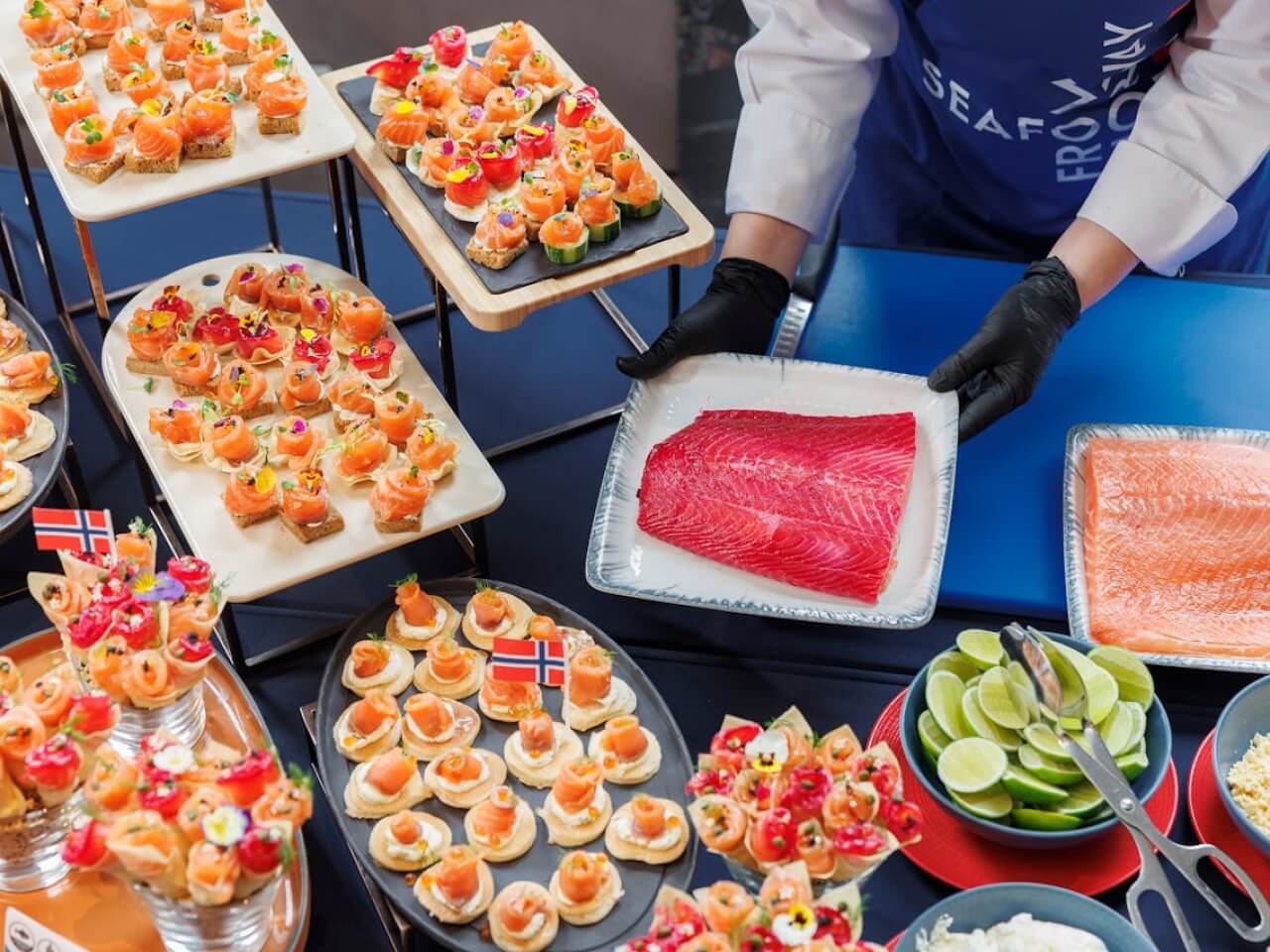 Catering display with salmon canapes, garnished bites, and a server holding trays of raw salmon