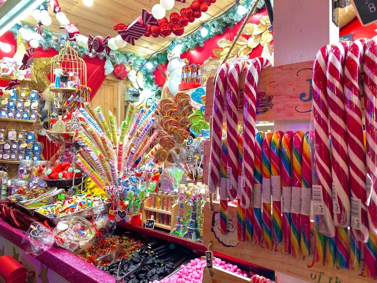 Confectionery stall packed with giant candy canes, rainbow lollipops, jars of sweets, and holiday decorations