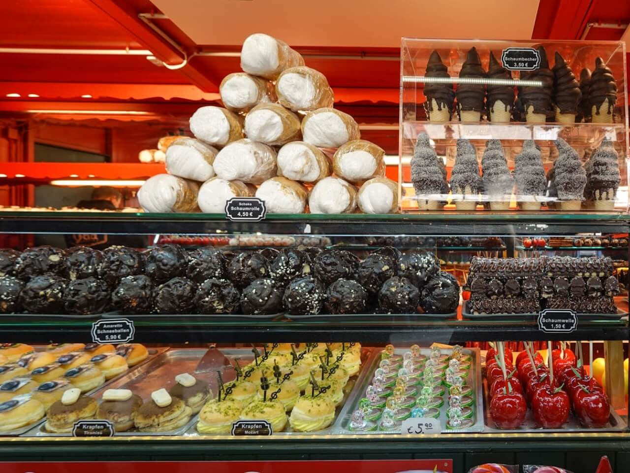 Dessert display case with cream rolls, chocolate pastries, layered cakes, and glossy red candied apples