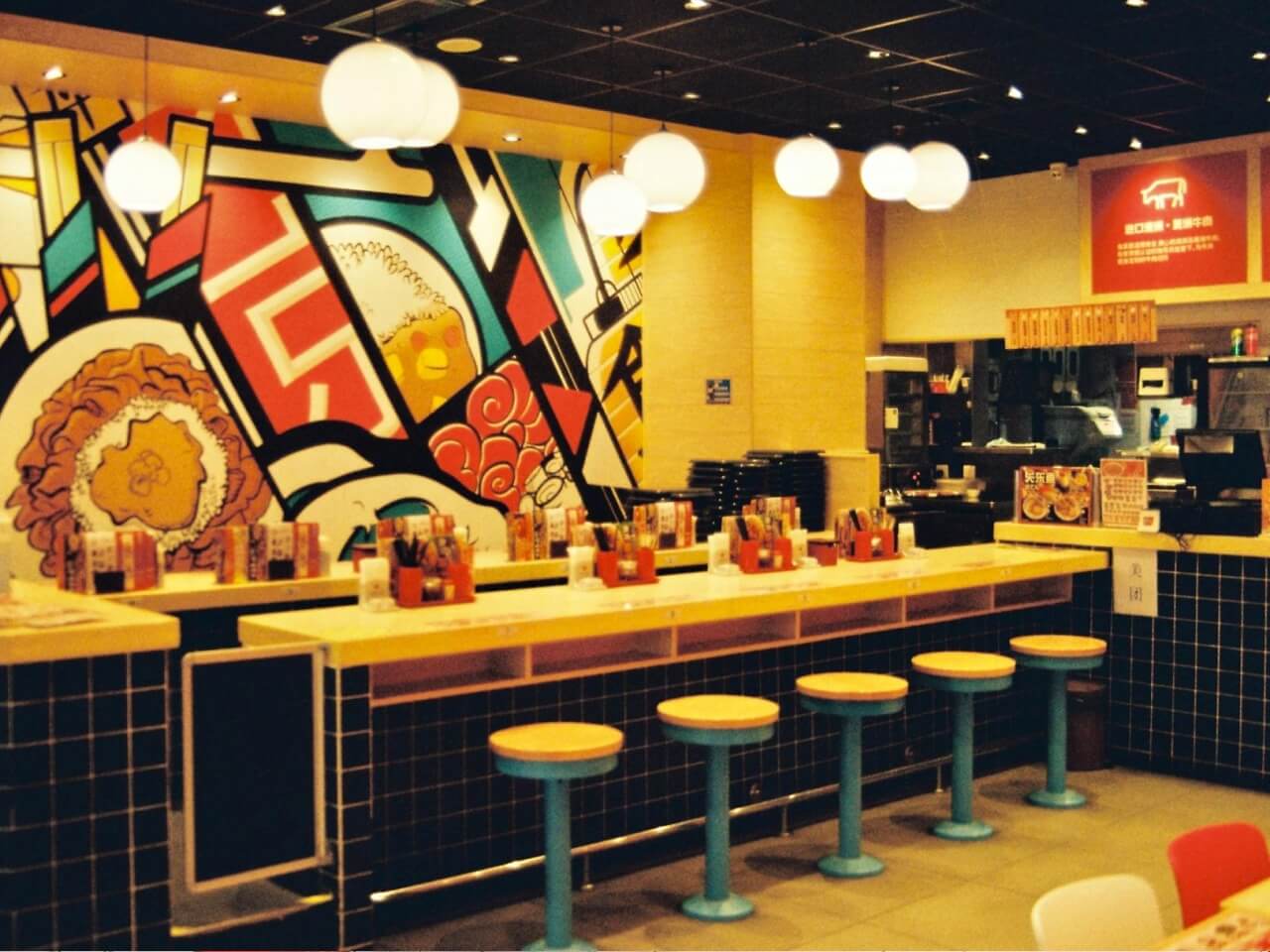 Fast food restaurant interior with counter seating, hanging globe lights, and a colorful wall mural