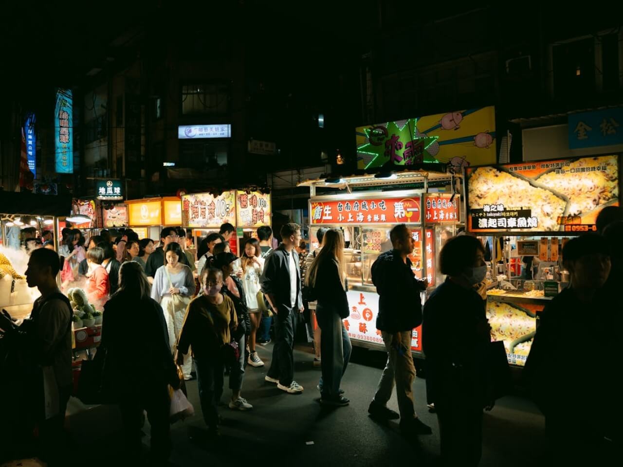 Crowded night market street with illuminated food stalls and customers walking past vendor counters